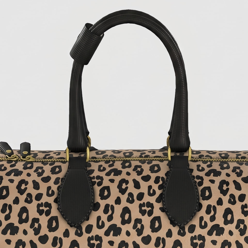 Close-up of a large Sahara leopard-print handbag with black leather handles and gold-tone hardware against a light gray background.