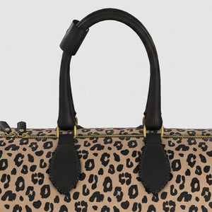 Close-up of a large Sahara leopard-print handbag with black leather handles and gold-tone hardware against a light gray background.