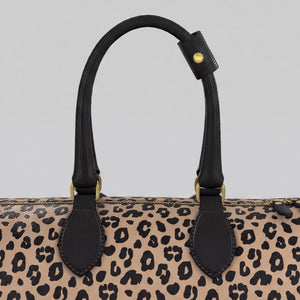 Close-up of a large Sahara leopard-print handbag with black leather handles and gold-tone hardware against a light gray background.
