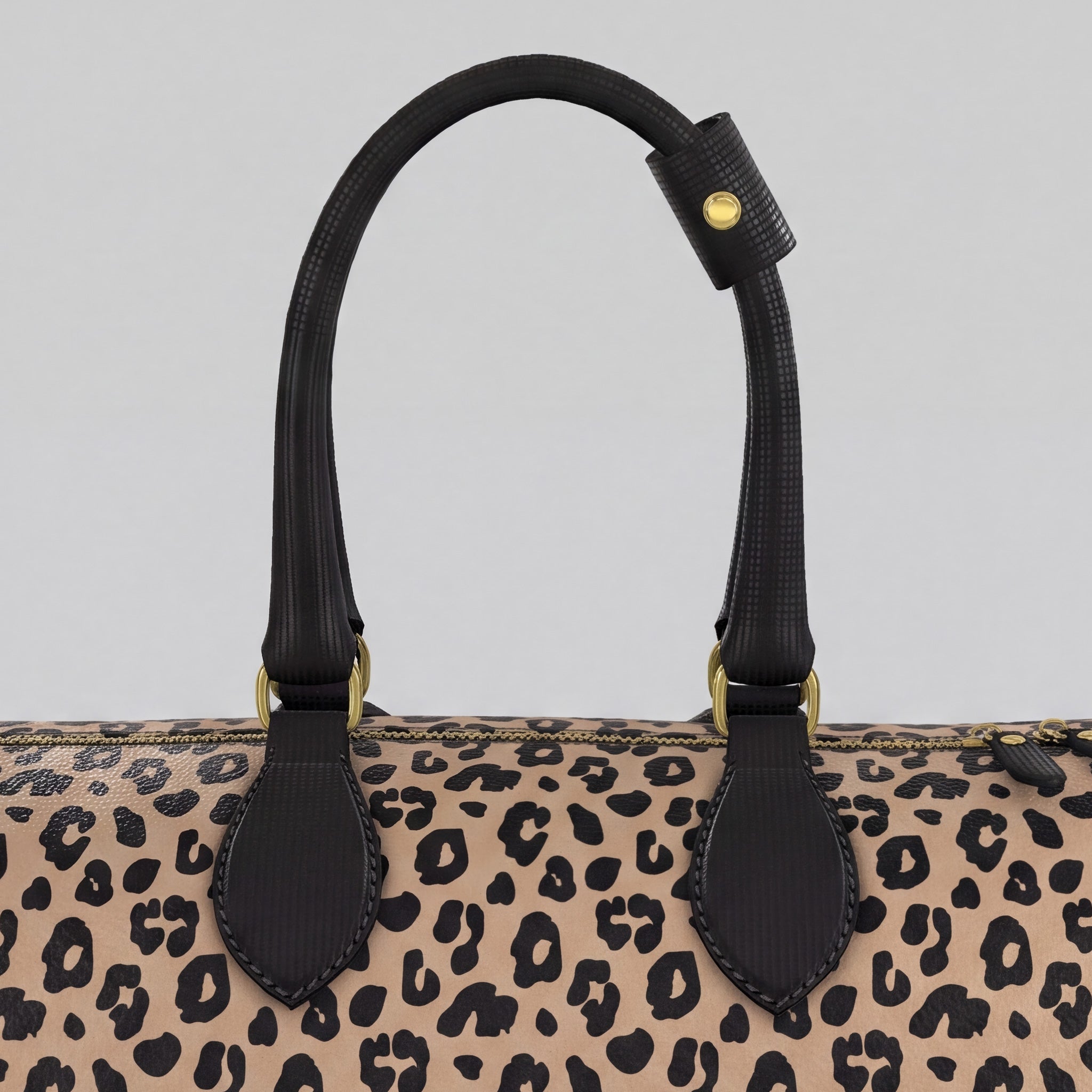 Close-up of a large Sahara leopard-print handbag with black leather handles and gold-tone hardware against a light gray background.