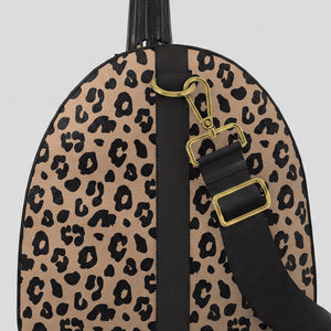 A close-up right view of a Sahara leopard print large duffel bag with black trim, a black top handle, and a black shoulder strap with gold-tone hardware, shown against a light gray background.