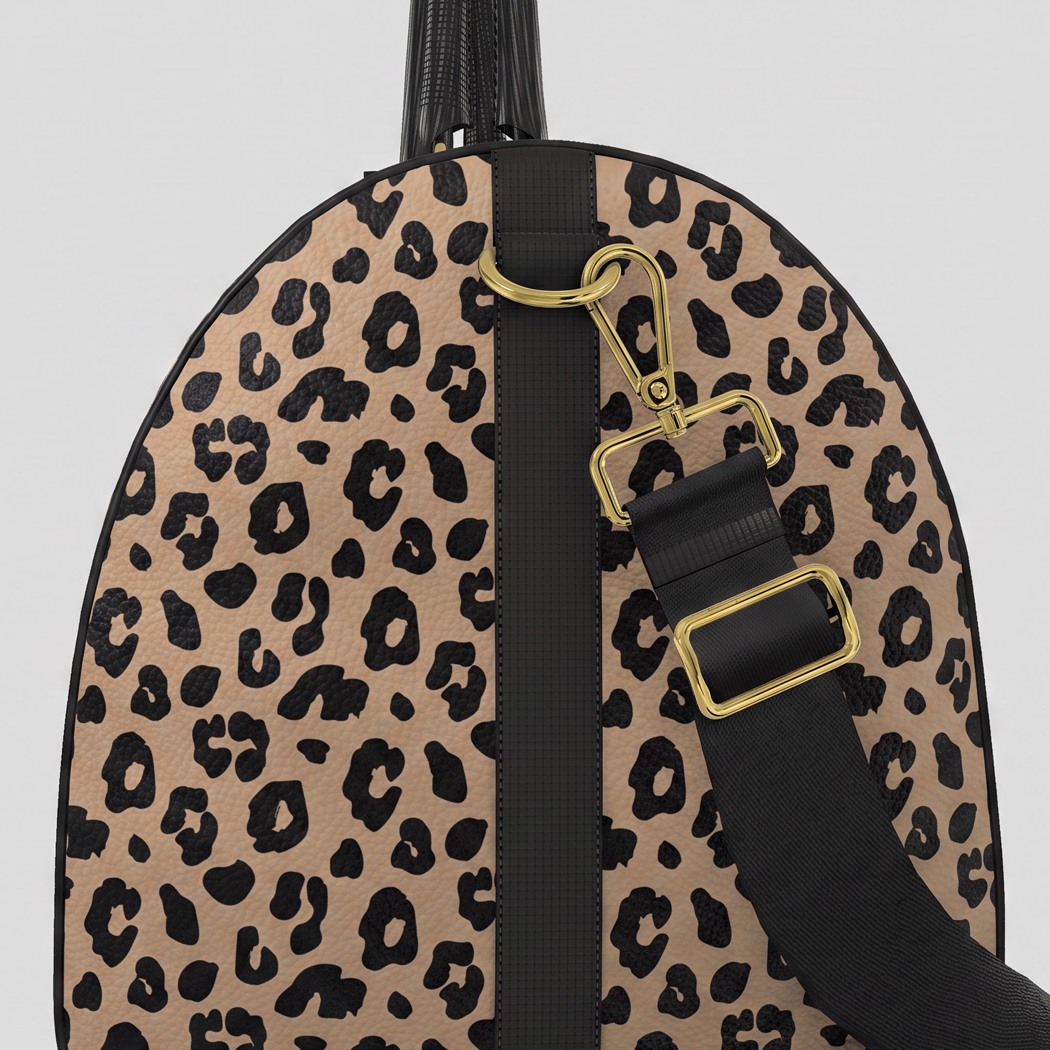 A close-up right view of a Sahara leopard print large duffel bag with black trim, a black top handle, and a black shoulder strap with gold-tone hardware, shown against a light gray background.
