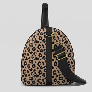 A right view of a Sahara leopard print large duffel bag with black trim, a black top handle, and a black shoulder strap with gold-tone hardware, shown against a light gray background.