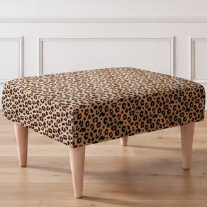 A close-up side view of an ottoman with a leopard print fabric top and four tapered light wood legs, set against a white paneled wall and light wood floor.