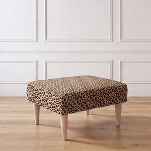A side view of an ottoman with a leopard print fabric top and four tapered light wood legs, set against a white paneled wall and light wood floor.
